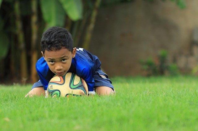 malý kluk ležící na fotbalovém míči